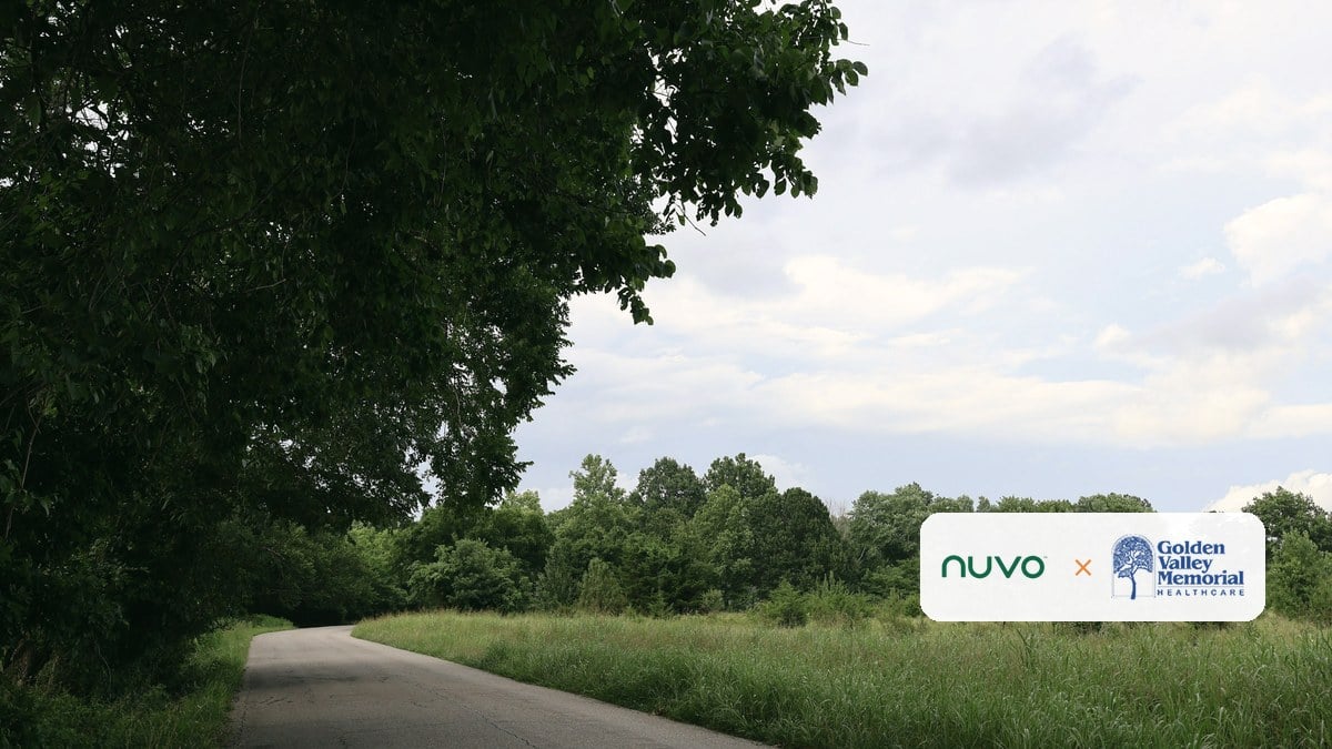 A country road running out of the trees into open fields near Joplin, Missouri, with the Nuvo and Golden Valley Memorial Healthcare logos