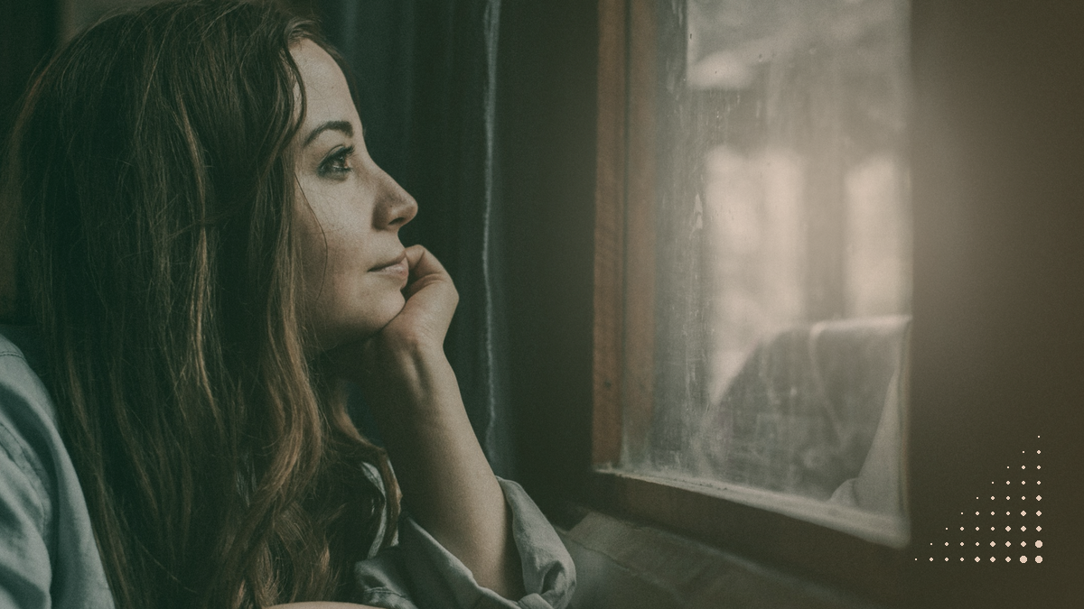 A woman sits by a dark window, chin on her hand, waiting
